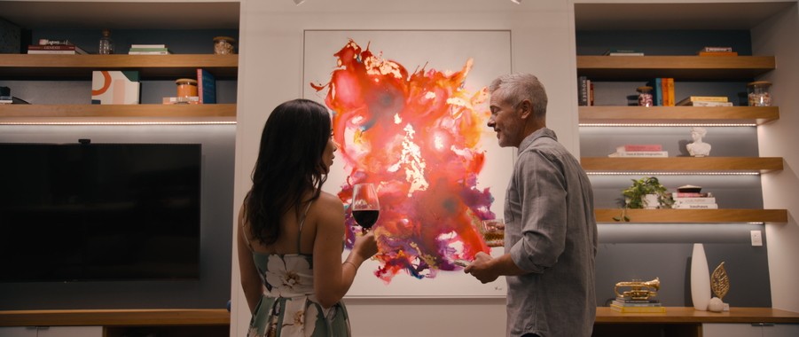 Two people drinking wine standing in front of a piece of abstract art illuminated by lighting design