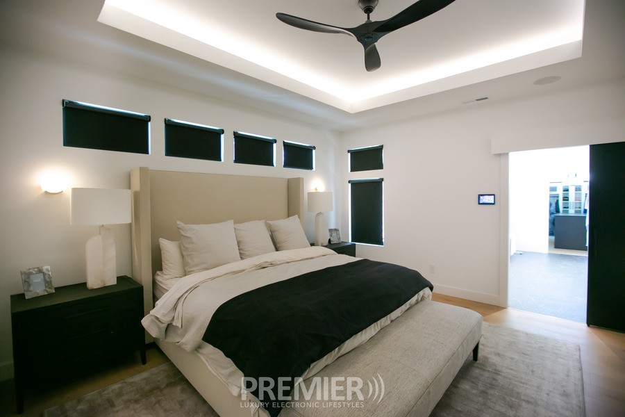 A bedroom with soft lighting and motorized shades fully lowered. 